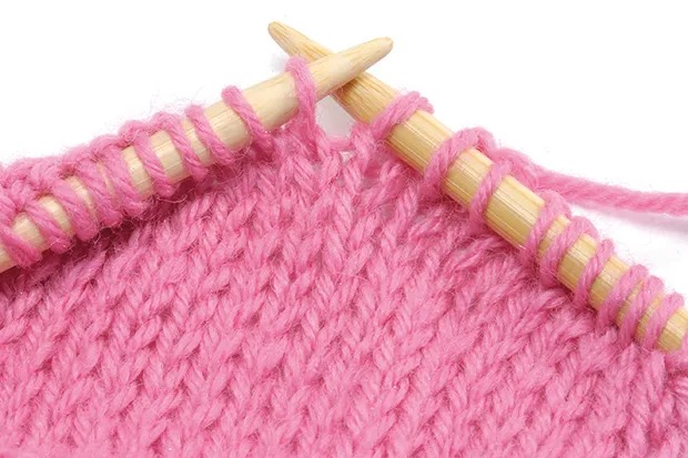 Knitting, pink wool on wooden needles